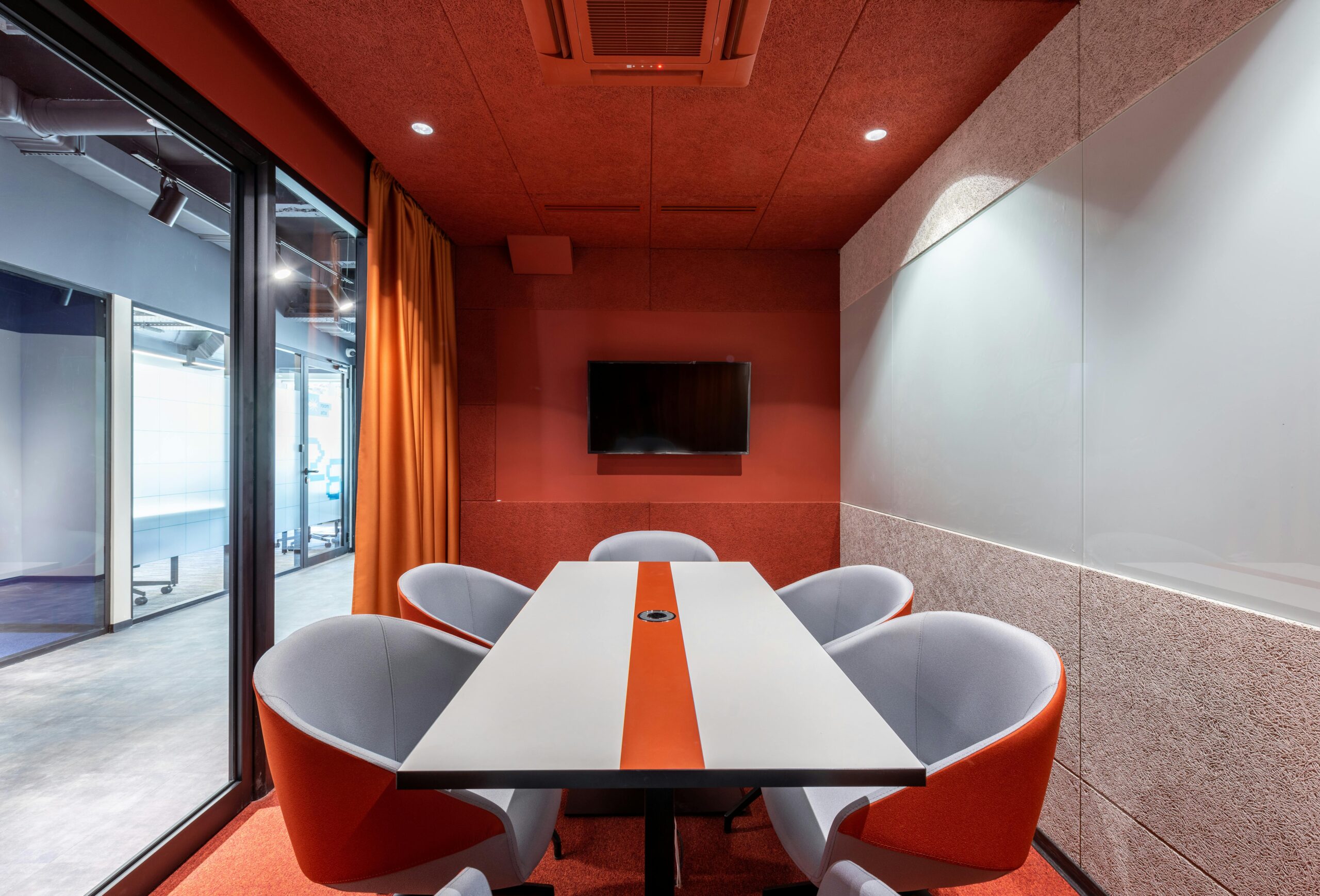 Stylish modern meeting room with orange accents, glass wall, and contemporary furnishings.